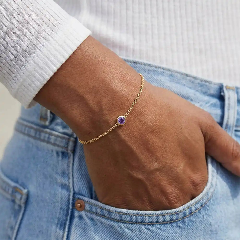 Model wearing bezel-set birthstone bracelet. silver variant--14K-yellow-gold variant--Amethyst