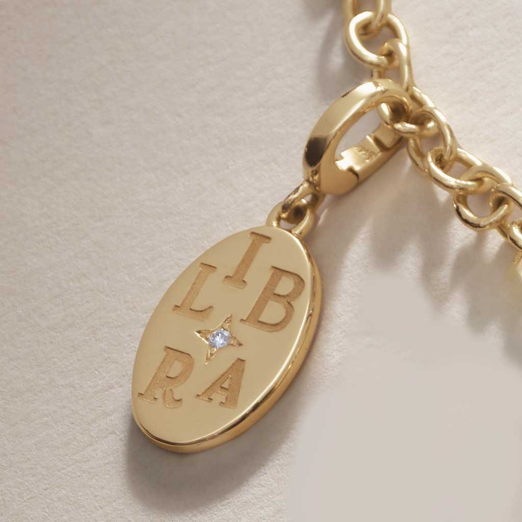 Gold Libra zodiac charm with a diamond on a beige background.