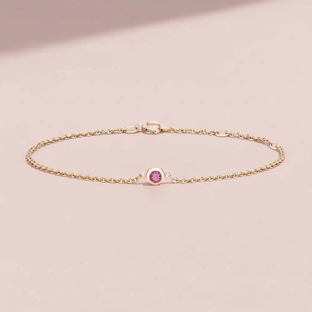Bezel-set tourmaline bracelet flatlay showing deep pink stone on curb chain yellow gold variant--14K-yellow-gold variant--Tourmaline
