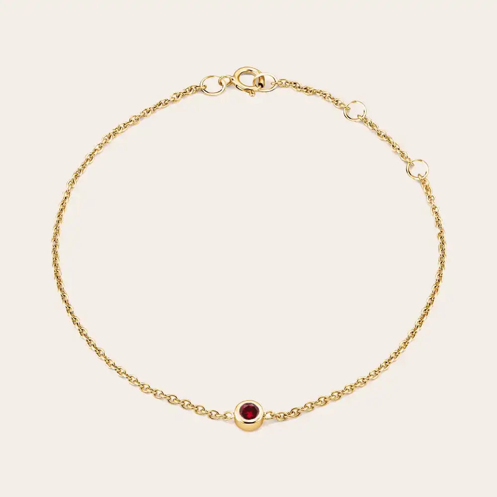 Bezel-set garnet bracelet flatlay showing deep red stone and curb chain yellow gold variant--14K-yellow-gold variant--Garnet