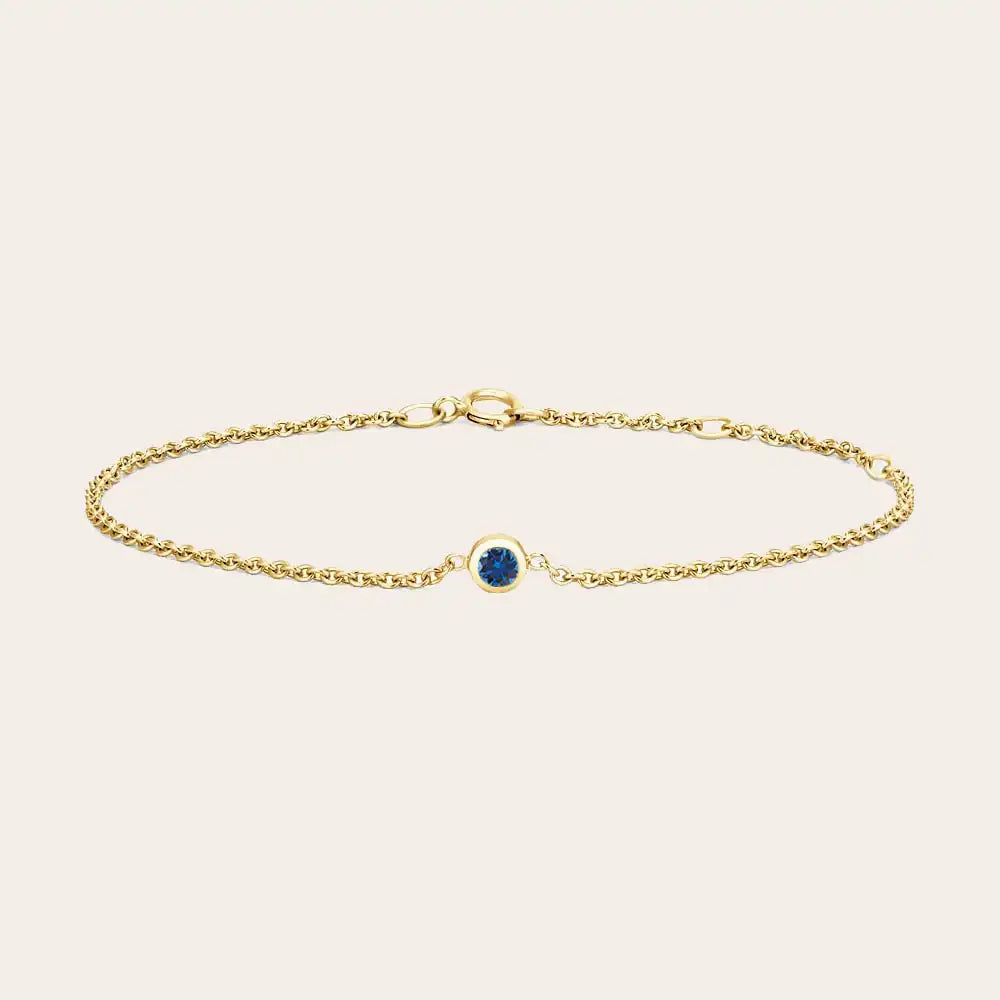 Bezel-set sapphire bracelet flatlay showing deep blue stone on curb chain
