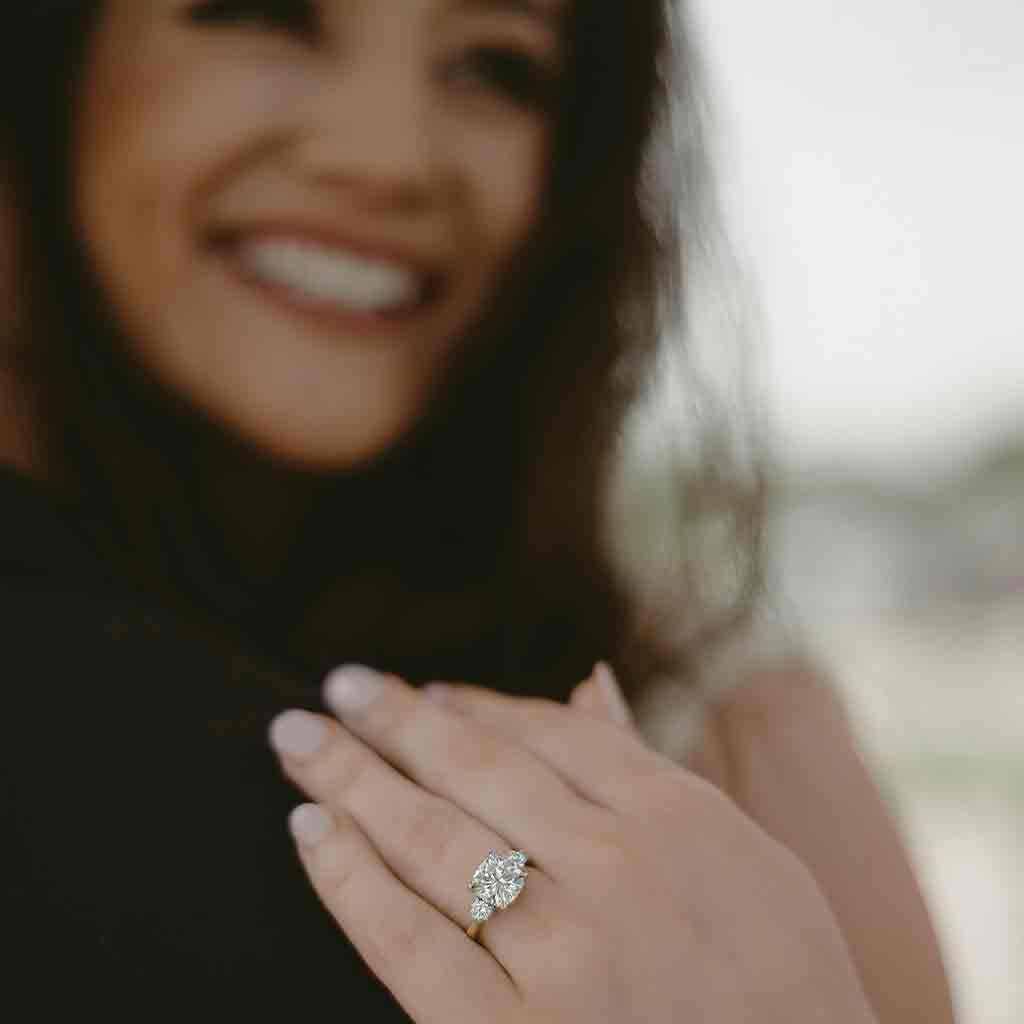 Three-stone engagement ring with round side stones in 14K gold, diamond center, on hand