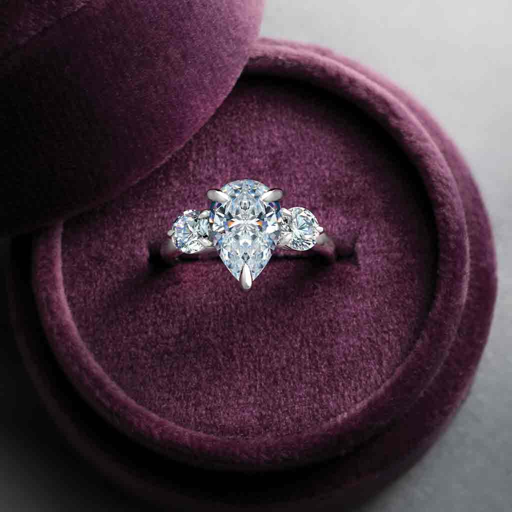 Three-stone engagement ring with round side stones in 14K gold, pear center, on hand