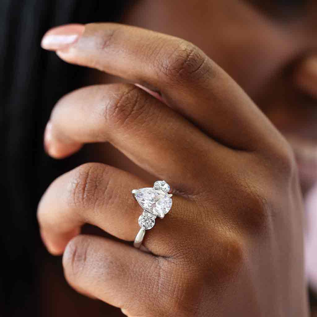 Three-stone engagement ring with round side stones in 14K gold, pear center, close-up of round side stones