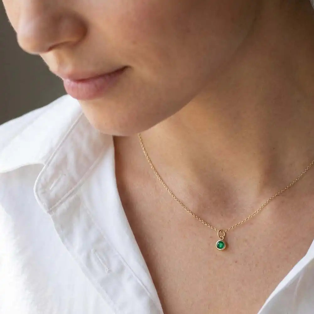 Emerald bezel charm necklace in 14K gold, close-up of natural green stone setting