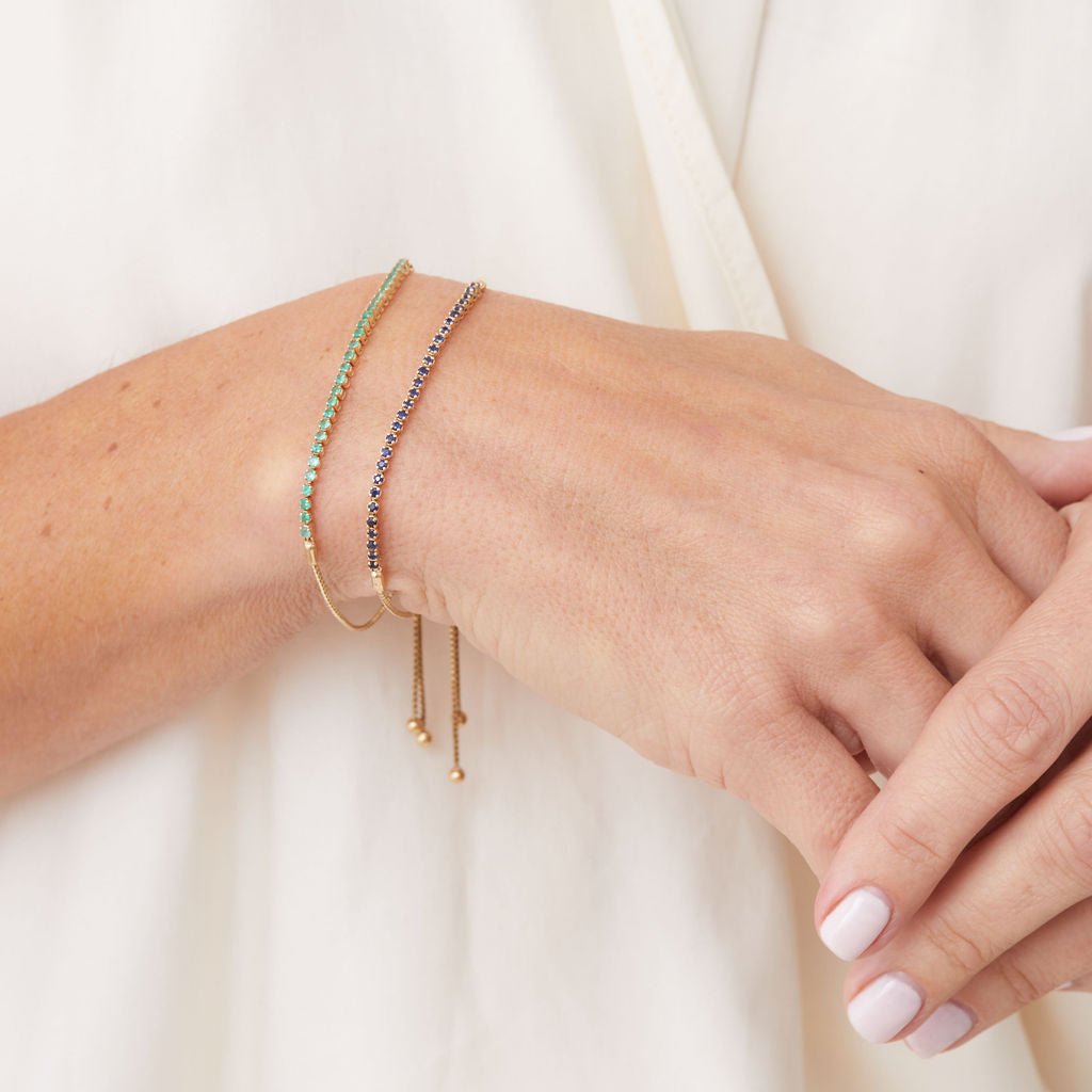 Gemstone adjustable tennis bracelets layered on model wrist, emerald and sapphire in gold