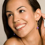 Woman wearing small faceted amethyst hoop earrings in yellow gold fill, deep purple gemstone with pink-violet flash, lifestyle portrait. all-groups