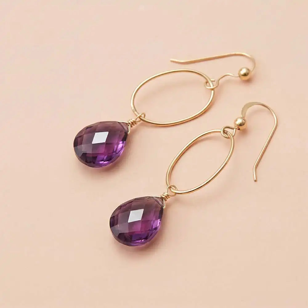 Faceted amethyst drop earrings in yellow gold fill, deep purple gemstone teardrop briolette suspended from slim oval gold link, blush background. all-groups