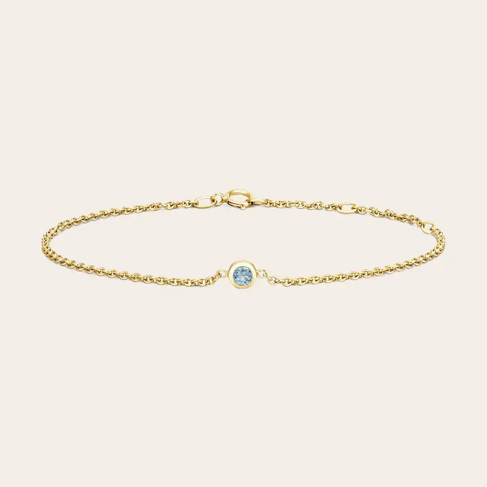 Bezel-set aquamarine bracelet flatlay showing pale blue stone on curb chain yellow gold variant--14K-yellow-gold variant--Aquamarine