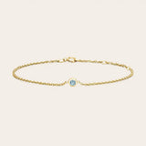 Bezel-set aquamarine bracelet flatlay showing pale blue stone on curb chain yellow gold variant--14K-yellow-gold variant--Aquamarine