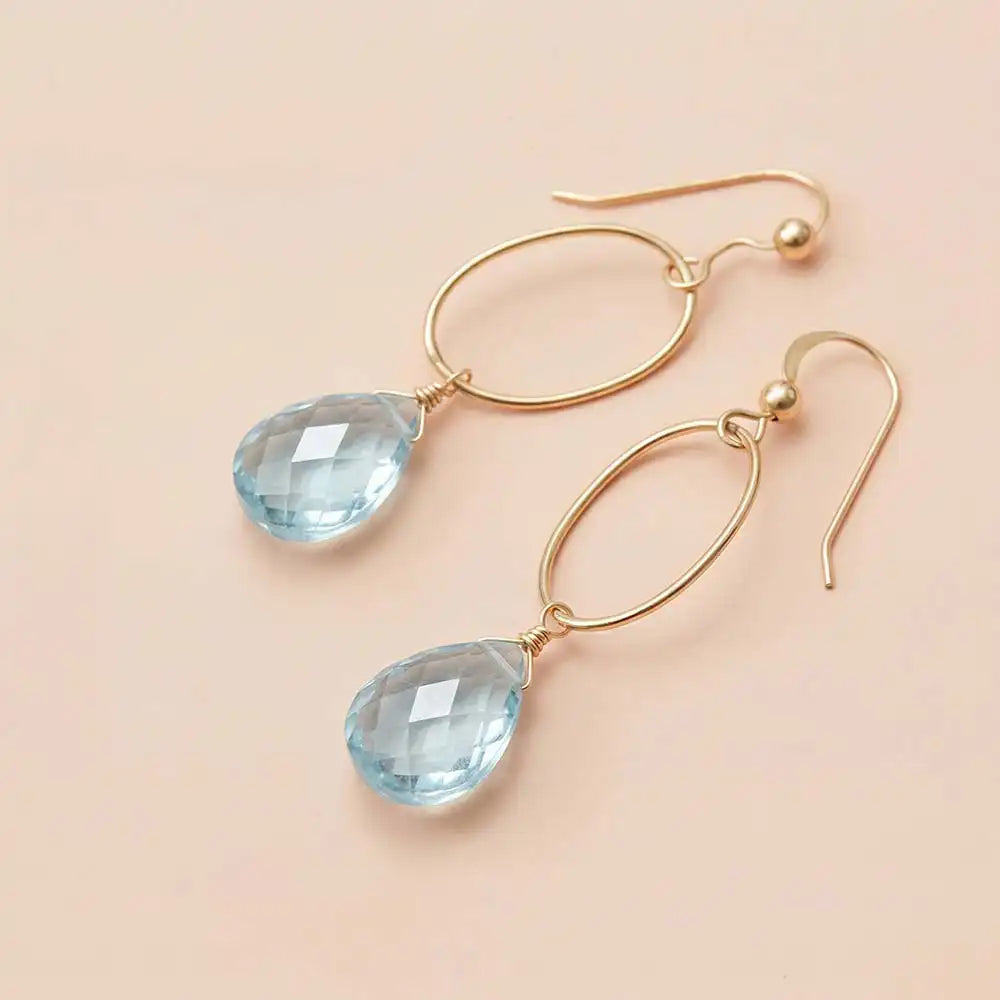 Faceted aquamarine drop earrings in yellow gold fill, pale sky-blue
gemstone teardrop briolette suspended from slim oval gold link,
blush background. all-groups