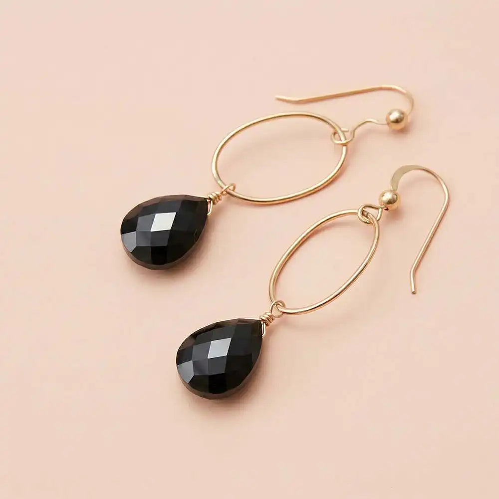 Faceted black sapphire drop earrings in yellow gold fill, deep black
gemstone teardrop briolette suspended from slim oval gold link,
blush background. all-groups