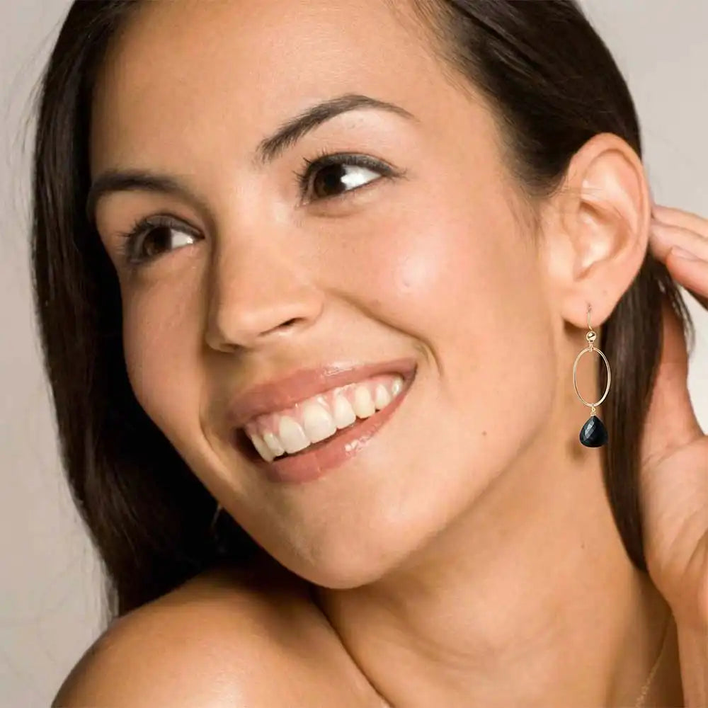Woman wearing small faceted black sapphire hoop earrings in yellow gold fill, deep black gemstone with subtle dark flash, lifestyle portrait. all-groups