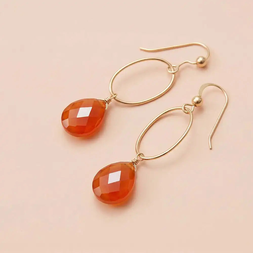 Faceted carnelian drop earrings in yellow gold fill, warm orange gemstone teardrop briolette suspended from slim oval gold link, blush background. all-groups