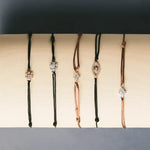 Stack of silk thread bracelets with mixed metal charms—initials, birthstones, and zodiacs in everyday lifestyle setting.