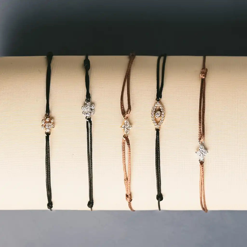 Stack of silk thread bracelets with mixed metal charms—initials, birthstones, and zodiacs in everyday lifestyle setting.
