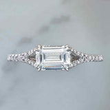 East-west French-set diamond halo engagement ring with emerald-cut center, editorial view