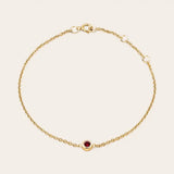 Bezel-set garnet bracelet flatlay showing deep red stone and curb chain yellow gold variant--14K-yellow-gold variant--Garnet