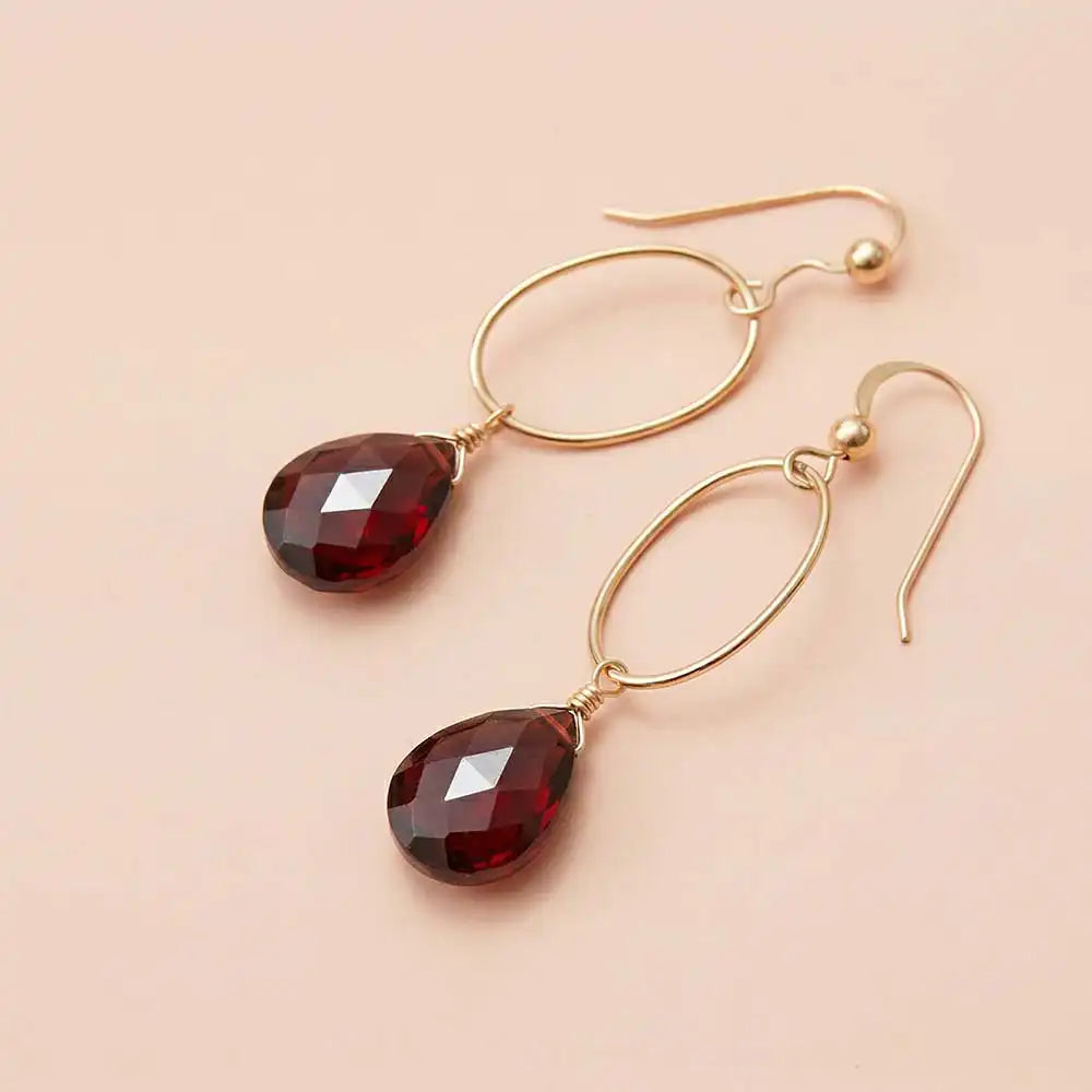 Faceted garnet drop earrings in yellow gold fill, rich burgundy-red
gemstone teardrop briolette suspended from slim oval gold link,
blush background. all-groups