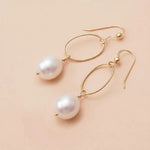 Pearl drop earrings in yellow gold fill, lustrous white pearl suspended from slim oval gold link, blush background. all-groups