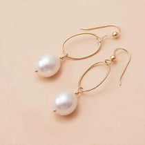 Pearl drop earrings in yellow gold fill, lustrous white pearl suspended from slim oval gold link, blush background. all-groups