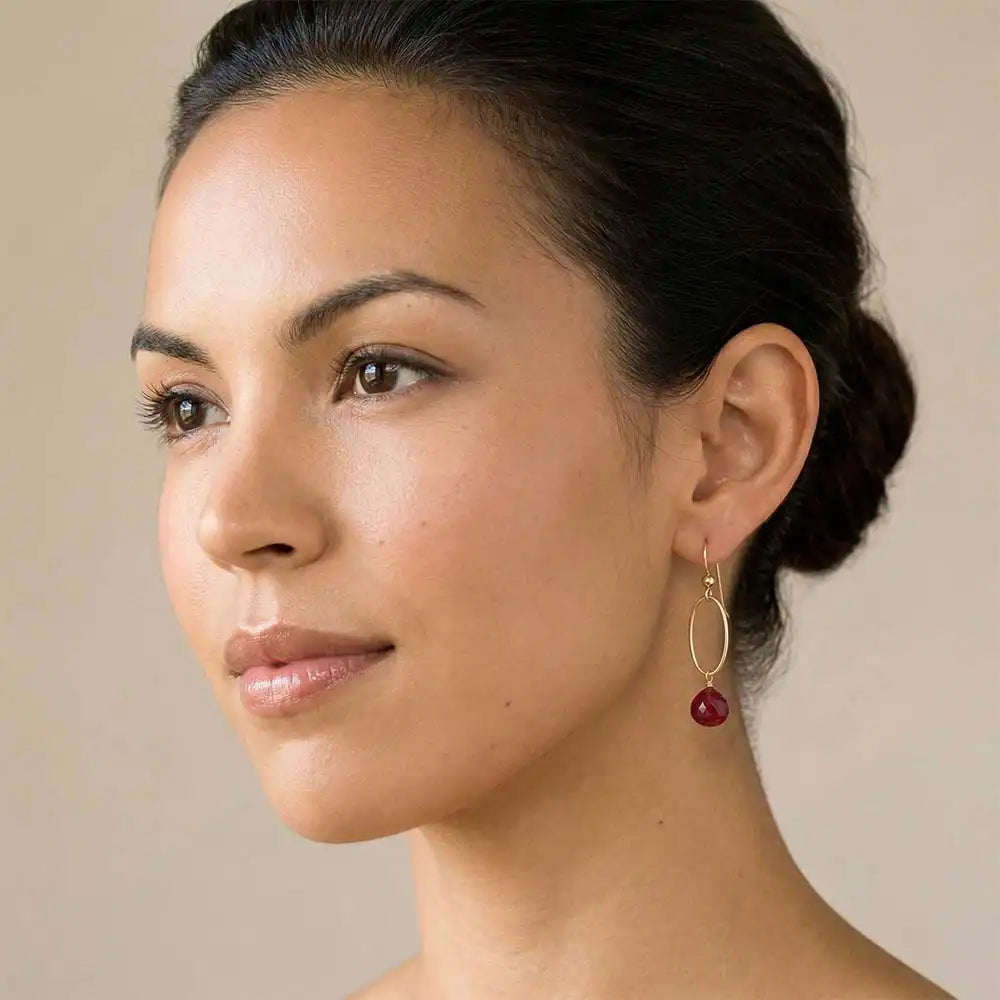 Woman wearing small faceted ruby hoop earrings in yellow gold fill, deep red gemstone with warm pink flash, lifestyle portrait. all-groups