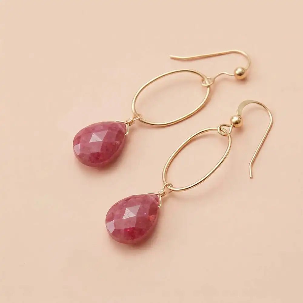 Faceted ruby drop earrings in yellow gold fill, deep red gemstone teardrop briolette suspended from slim oval gold link, blush background. all-groups