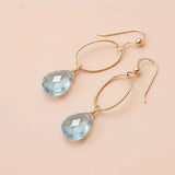 Faceted Swiss blue topaz drop earrings in yellow gold fill, bright medium-blue gemstone teardrop briolette suspended from slim oval gold link, blush background. all-groups