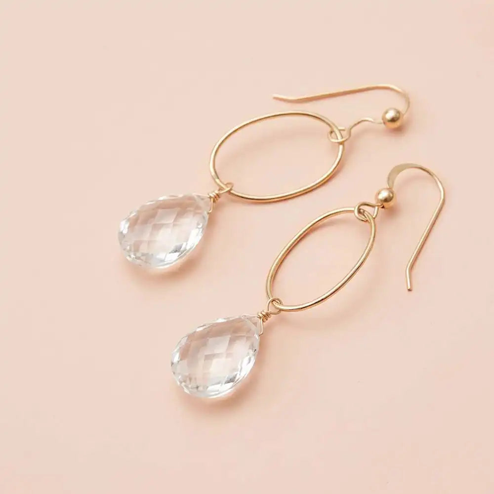 Faceted white topaz drop earrings in yellow gold fill, clear brilliant gemstone teardrop briolette suspended from slim oval gold link, blush background. all-groups