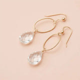 Faceted white topaz drop earrings in yellow gold fill, clear brilliant gemstone teardrop briolette suspended from slim oval gold link, blush background. all-groups