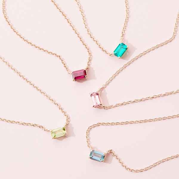 Multiple emerald-cut birthstone necklaces styled together, editorial layering shot